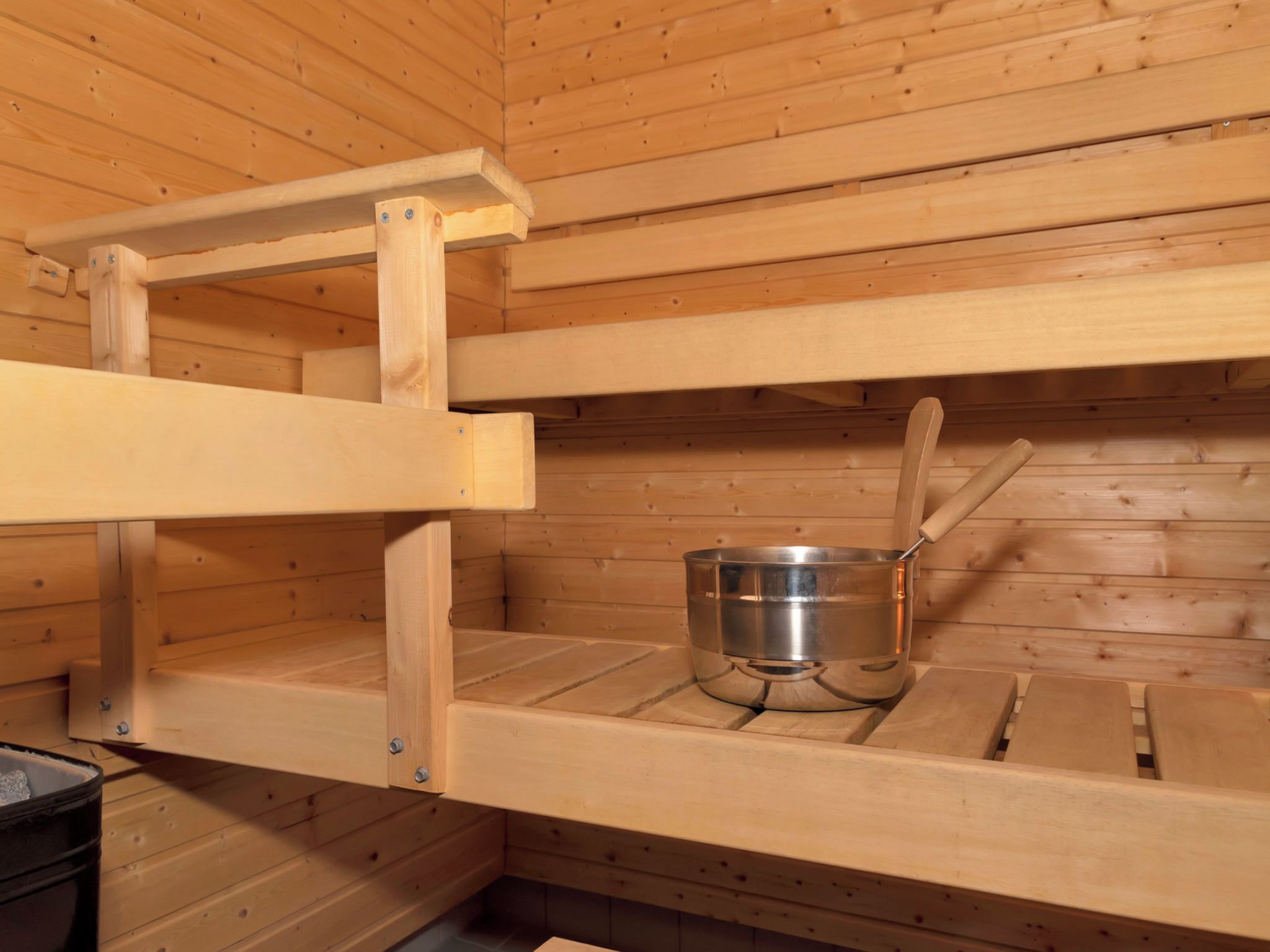 A sauna room with wooden walls and a metal basin.