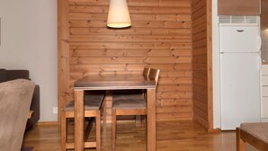 A wooden dining table with chairs, a hanging light fixture, and a white refrigerator in a room with wooden paneling and a wooden floor.