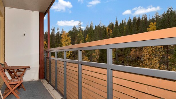 A balcony with a view of a forest, a wooden table, and a chair.