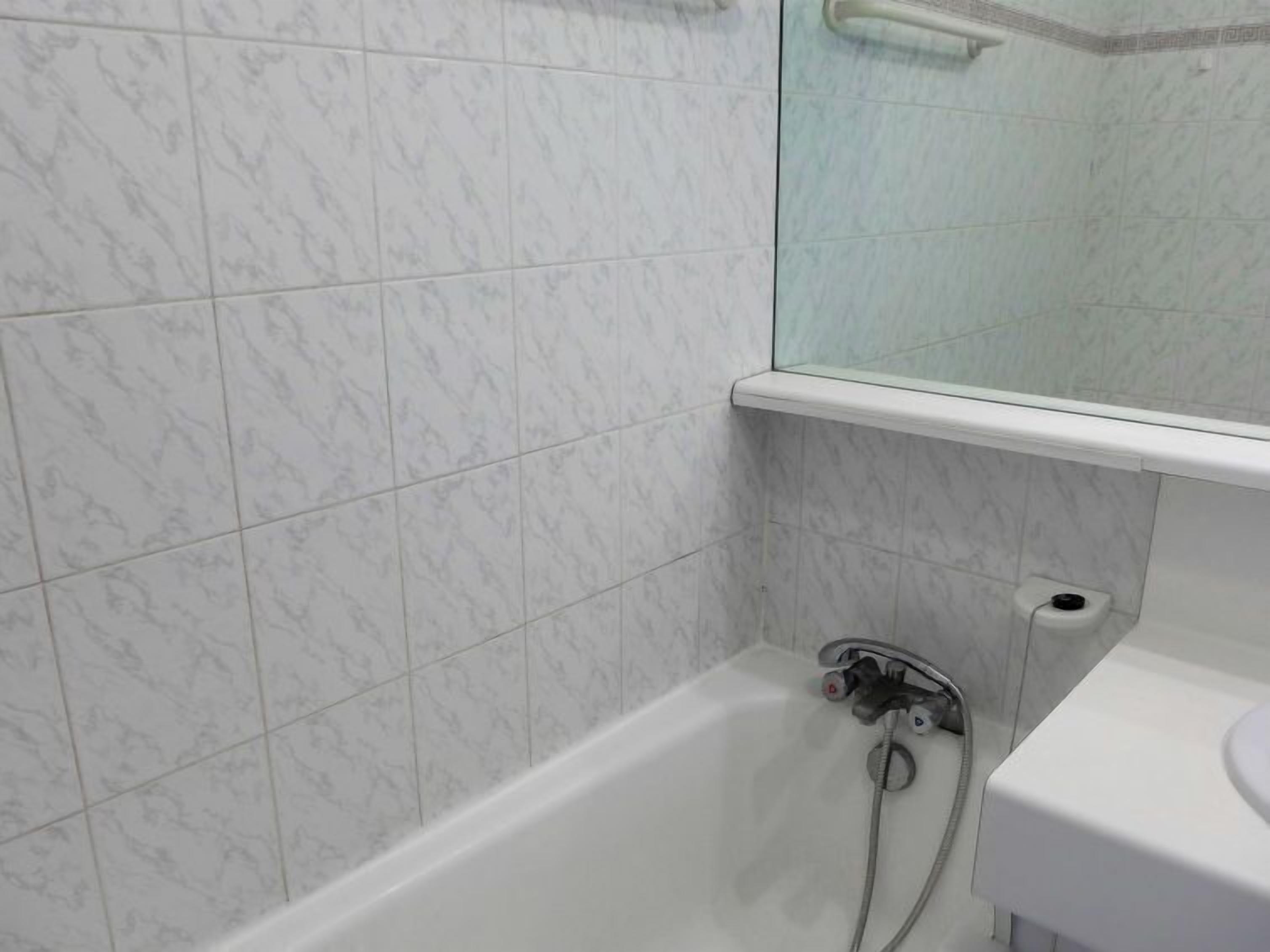 Ein Badezimmer mit weißen Marmorfliesen, einer weißen Badewanne, einer Duschkabine aus Glas und einem weißen Waschbecken.