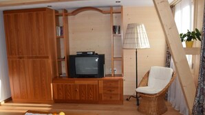 A cozy living room with a wooden entertainment unit, a television, a wicker chair, and a small table with fruit. - Däpp # 2 by Interhome (Lenk)