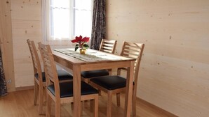A wooden dining table with four chairs, a vase with a red flower, and a window with curtains. - Däpp # 2 by Interhome (Lenk)