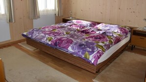 A bedroom with a wooden bed, a nightstand, a lamp, and a window with curtains. - Däpp # 2 by Interhome (Lenk)