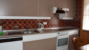 A compact kitchen with a dishwasher, stove, oven, and a coffee maker on the counter. - Däpp # 2 by Interhome (Lenk)