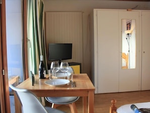 Ein Zimmer mit Holztisch, gedeckt für zwei Personen, einem Fernseher und einem Kleiderschrank.