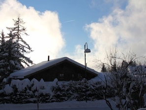 Ein mit Schnee bedecktes Blockhaus mit geneigtem Dach, umgeben von schneebedeckten Bäumen und Sträuchern.
