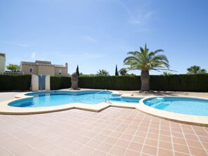 Una piscina de forma singular, rodeada por una terraza con azulejos y palmeras.