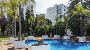 Un espace piscine doté d’une terrasse en bois, de chaises longues blanches et de palmiers.