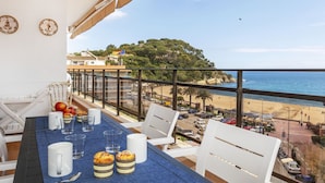 Un balcon avec une table dressée pour deux personnes, donnant sur une plage et une colline boisée.