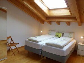 Une chambre avec un puits de lumière, deux lits, une chaise et des lampes de chevet.
