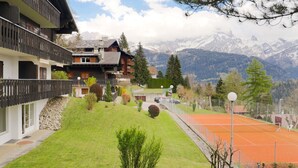 A chalet-style building with a balcony, a tennis court, and a mountainous backdrop. - Regina B9 by Interhome (Villars)