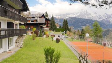 Ein Chalet mit Balkon, Tennisplatz und Bergblick.