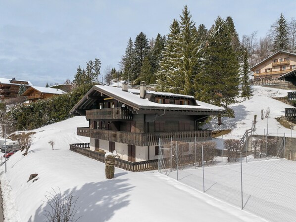 A chalet-style building with a wooden facade, a balcony, and a snow-covered roof.