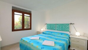 A bedroom with a bed, two bedside tables, a window, and a wall-mounted light fixture. - Tritone by Interhome (Porto Istana)