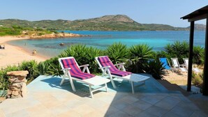 A beachside patio with lounge chairs and a pool, overlooking a clear blue sea and distant hills. - Tritone by Interhome (Porto Istana)
