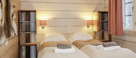 Une chambre avec deux lits, des murs en bois et une fenêtre ornée de rideaux rouges.