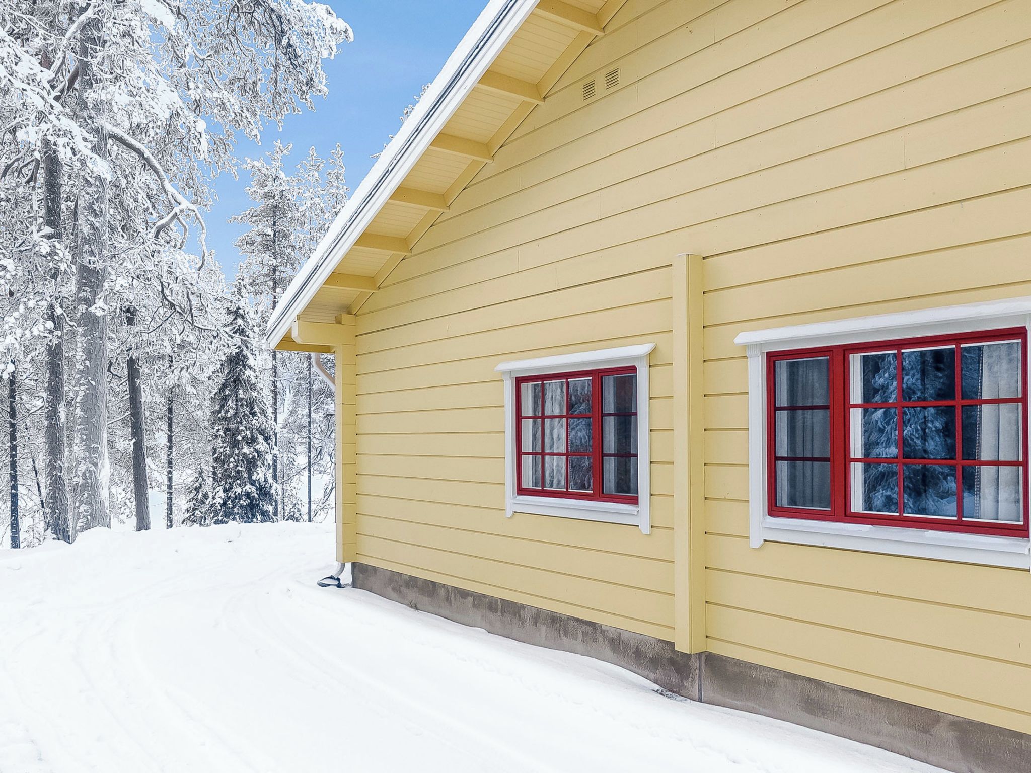 Een geel huis met twee ramen, omgeven door met sneeuw bedekte bomen.