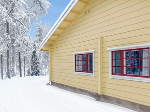Una casa amarilla con dos ventanas, rodeada de árboles cubiertos de nieve.