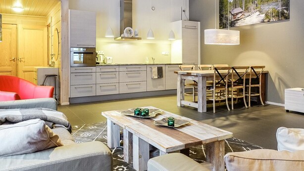 A modern kitchen with white cabinets, a dining area with a wooden table and chairs, and a large window with a view of trees. - Sallan panparkstie 14 b by Interhome (Salla)