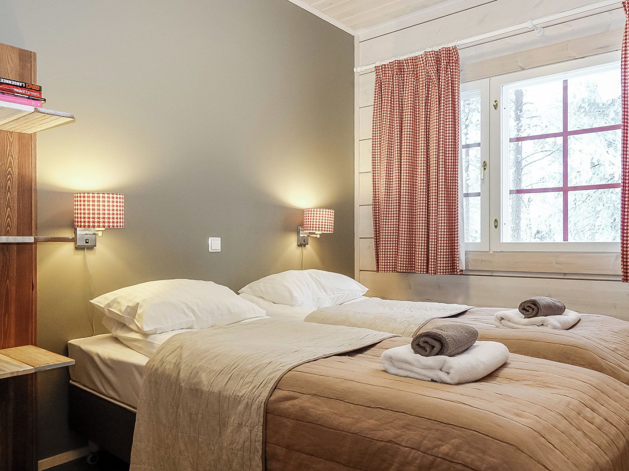 Ein Hotelzimmer mit zwei Betten, einem Fenster mit Vorhängen, Nachttischlampen und einer Holzablage mit Büchern.