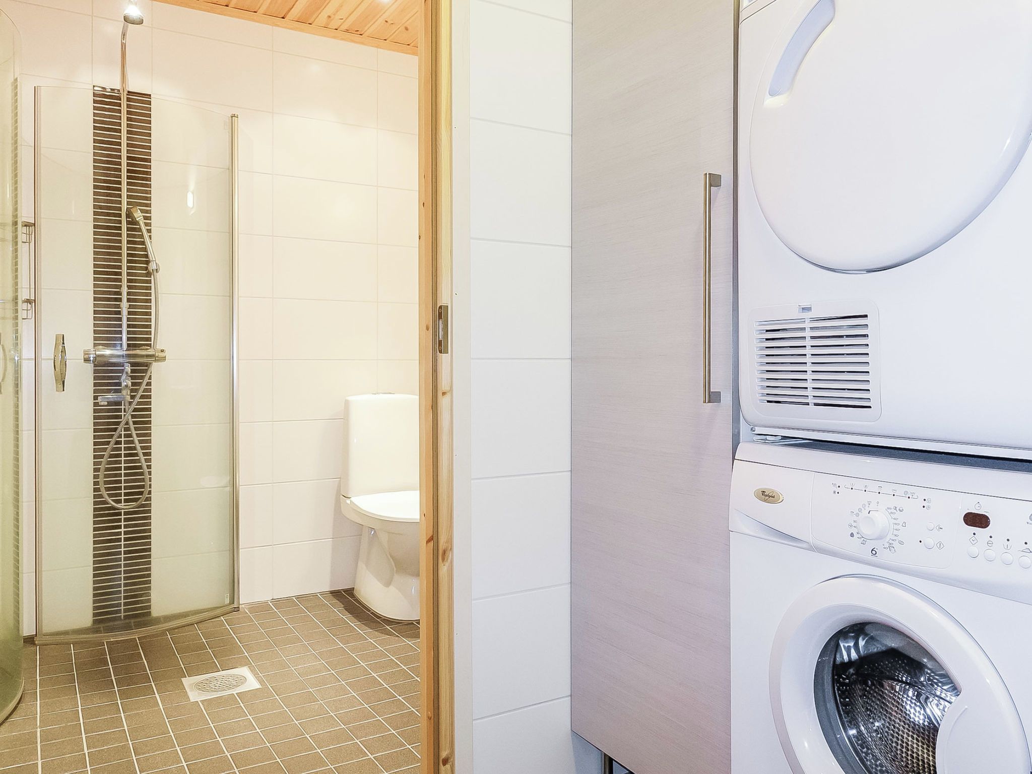 A modern bathroom with a glass-enclosed shower, a toilet, and a built-in washing machine.