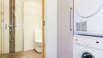 A modern bathroom with a glass-enclosed shower, a toilet, and a built-in washing machine.