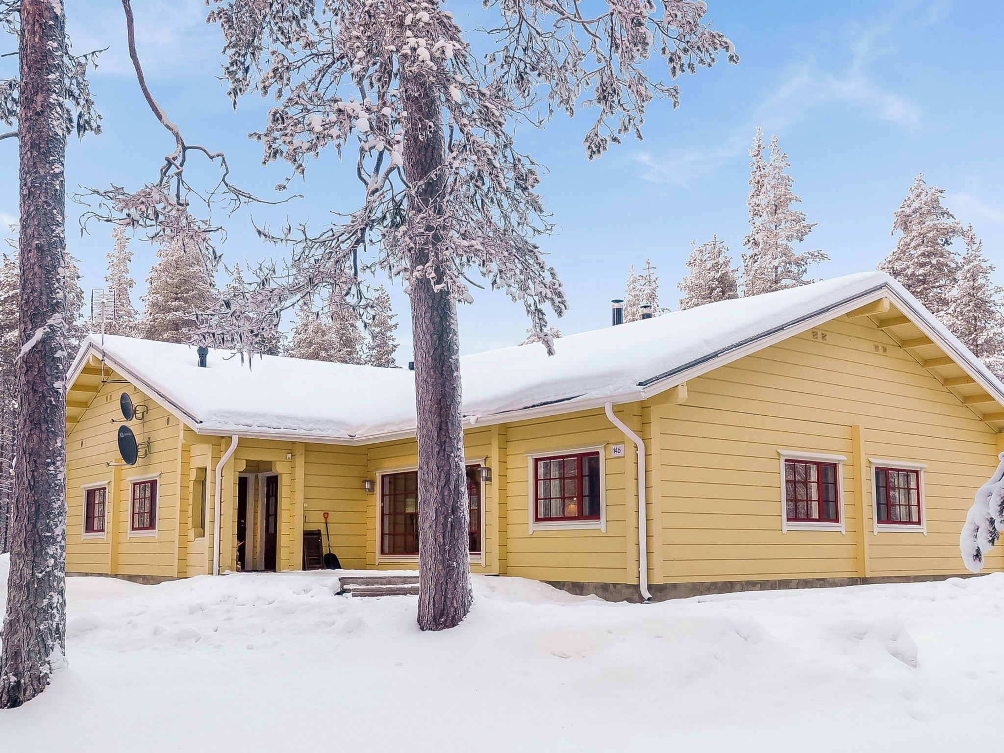 A yellow cabin with a snow-covered roof, surrounded by trees.