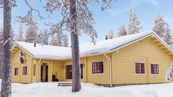 A yellow cabin with a snow-covered roof, surrounded by trees.