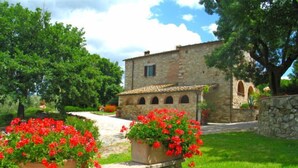 Un edificio in pietra con tetto in tegole, immerso nel verde e circondato da fiori rossi.