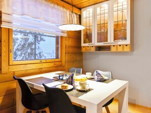 A dining area with a table set for two, a window with a view of snow-covered trees, and wooden cabinetry above the table.