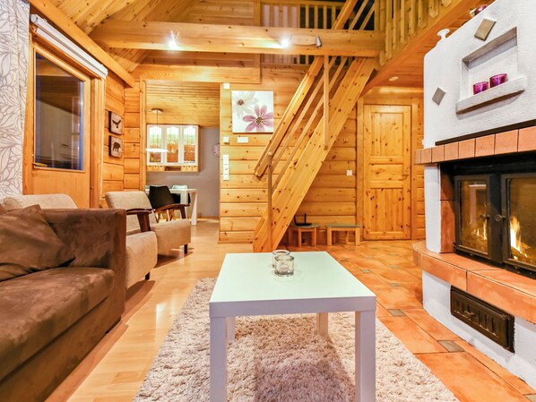 A cozy log cabin interior with a fireplace, wooden walls, a sofa, and a dining area.