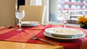 A dining table with two plates and two wine glasses, a fork, and a red table runner.