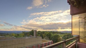 A building with multiple floors, a balcony with a metal railing, and a view of a landscape with trees and distant hills.
