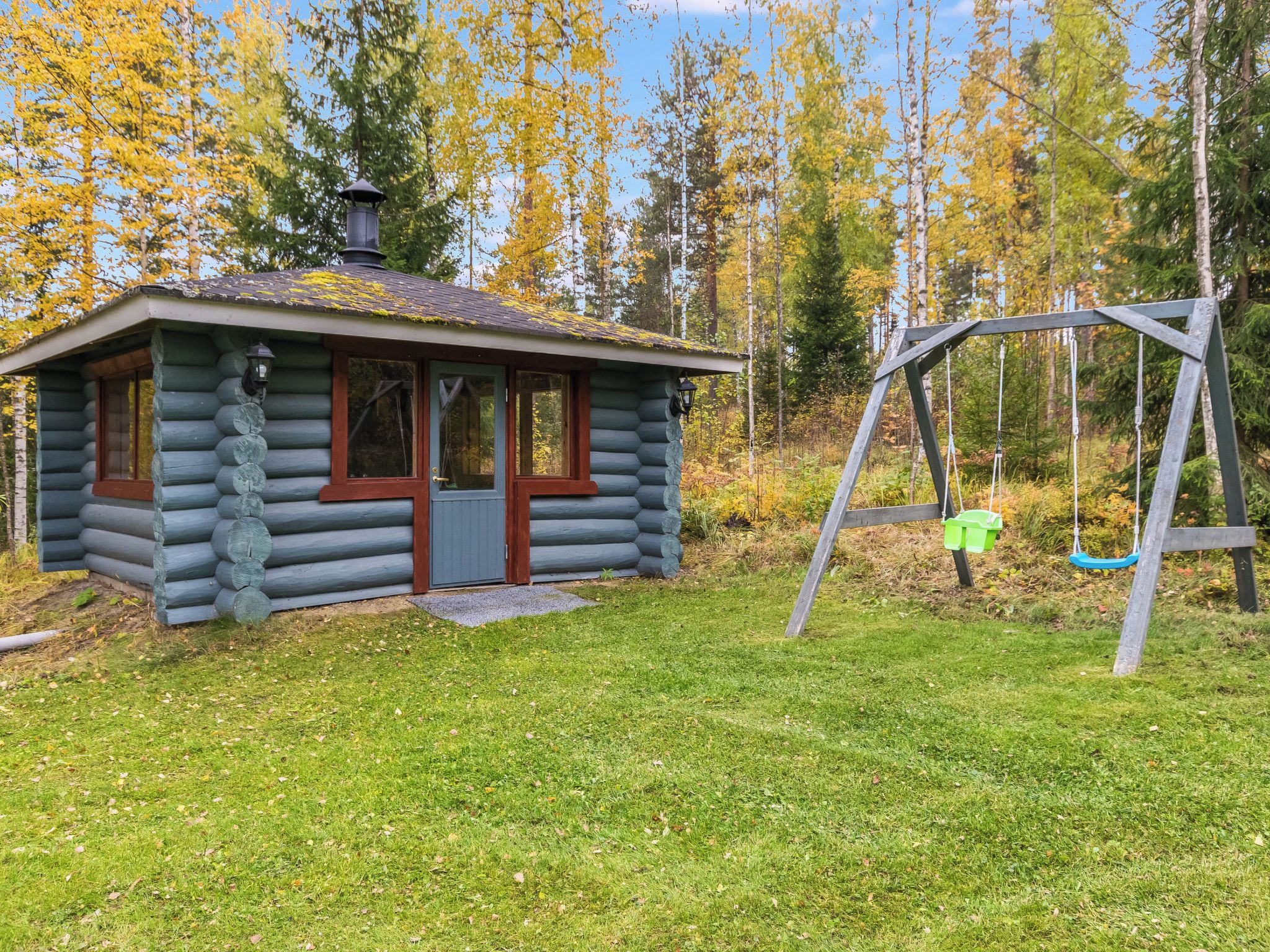 A log cabin with a porch and a swing set in a wooded area.