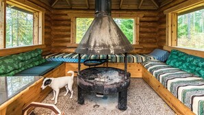 Interior de una cabaña con estufa de leña, paredes de madera y ventana con vistas a un bosque.