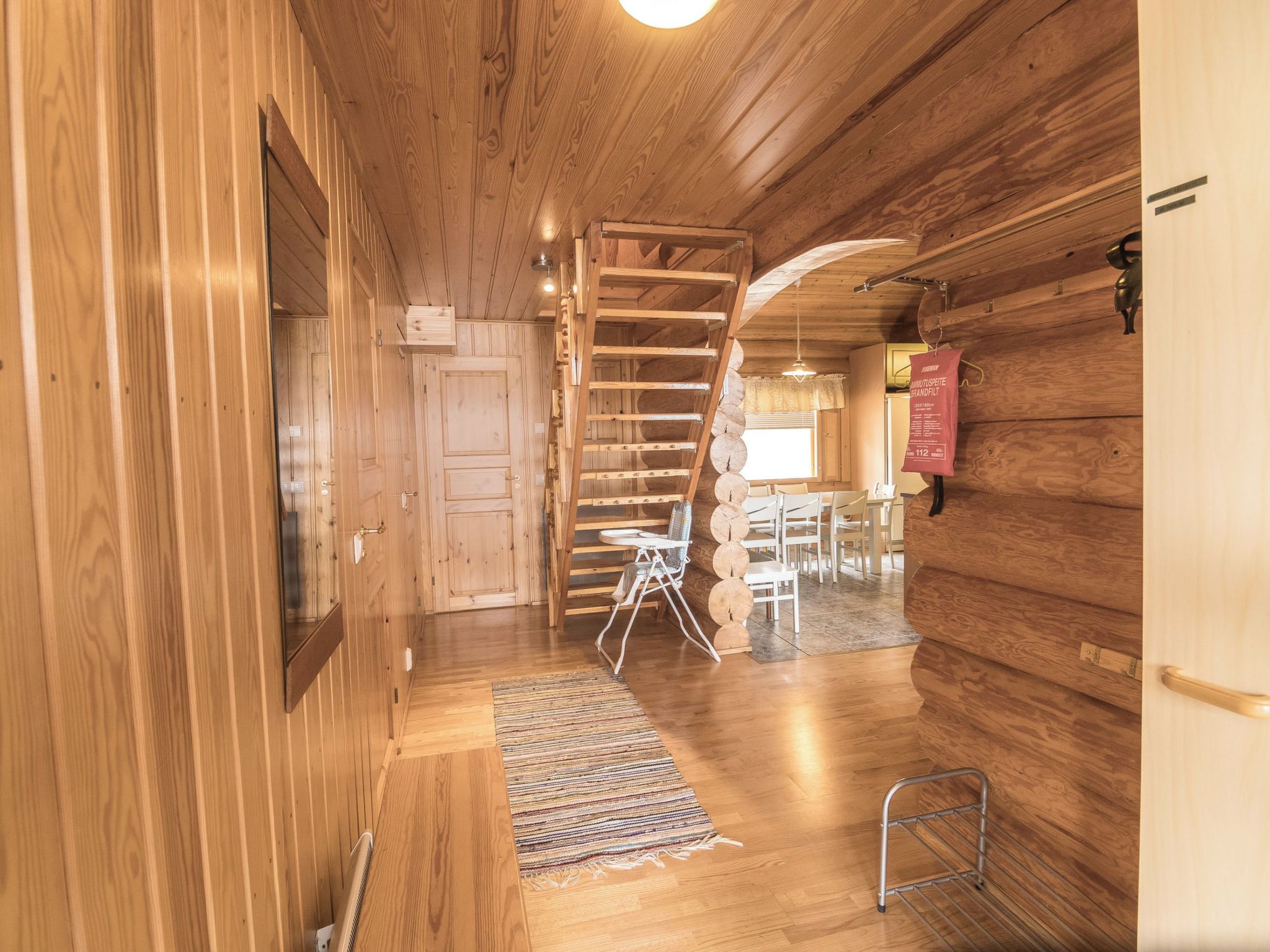 A wooden interior with a wooden staircase, a dining area with chairs and a table, and a small metal stool.