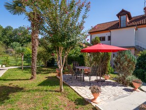 A patio with outdoor furniture, a red umbrella, and a house with a tiled roof. - Vacation home Franjo by Interhome (Opatija/Ika)