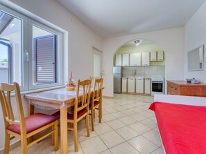 Une cuisine compacte avec un coin repas, un lit et une fenêtre équipée de stores.