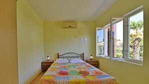 Une chambre avec un lit, deux tables de chevet avec des lampes, une fenêtre donnant sur un paysage verdoyant et un climatiseur fixé au mur.