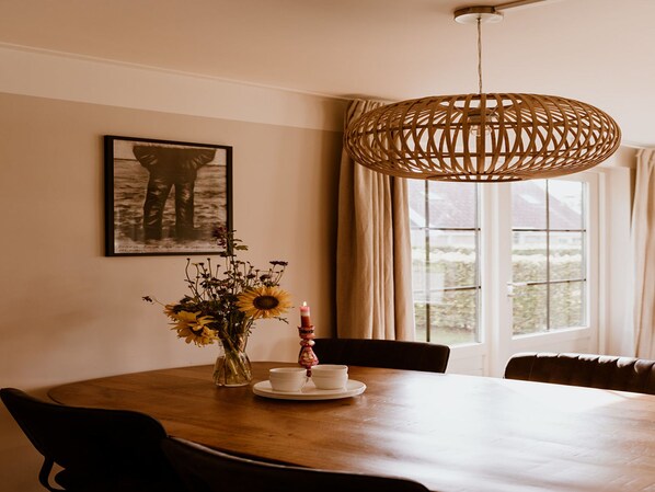 A dining area with a wooden table, chairs, a vase with flowers, a candle, and a framed picture on the wall.