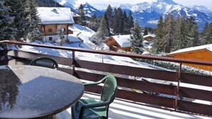A balcony with a table and chairs overlooking a snowy mountain landscape with houses and trees. - Schuss 23 by Interhome (Villars)