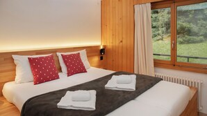 A neatly made bed with white and red pillows, a grey blanket, and two folded towels. - Schuss 23 by Interhome (Villars)