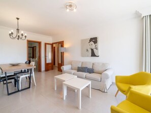 Een moderne woonkamer met een eethoek, een bank, een gele fauteuil en een schilderij aan de muur.