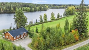 Une maison avec un toit sombre, entourée d’un paysage verdoyant et luxuriant et d’un lac.