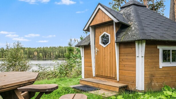 Une cabane en bois dotée d’une porte hexagonale, d’une petite fenêtre et d’une terrasse avec des tables de pique-nique.