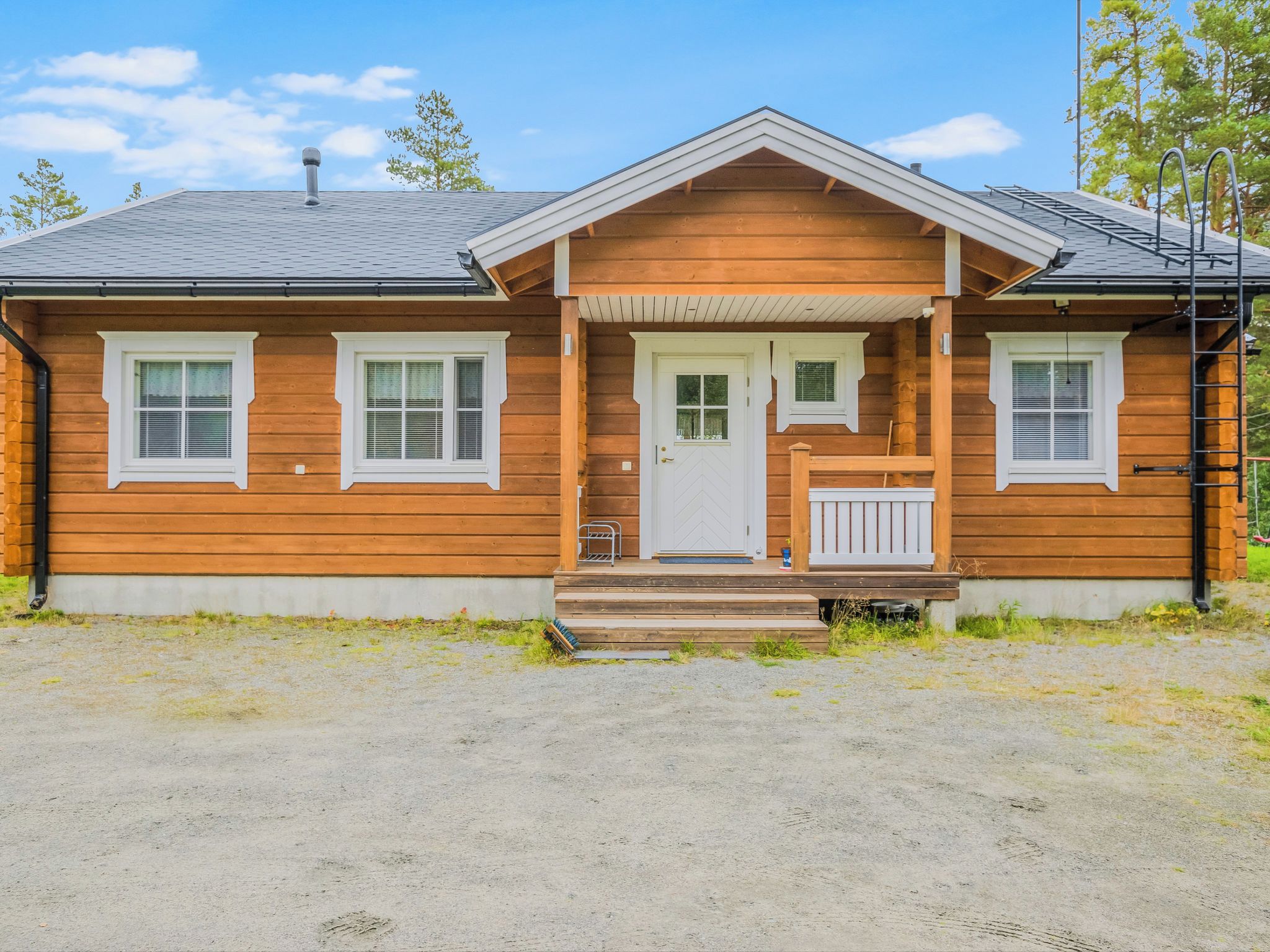 A two-story wooden house with a front porch, a chimney, and a gravel driveway.