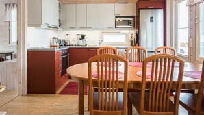 Une cuisine compacte avec des meubles blancs, un four à micro-ondes et un réfrigérateur. On y trouve une table à manger en bois, accompagnée de quatre chaises.
