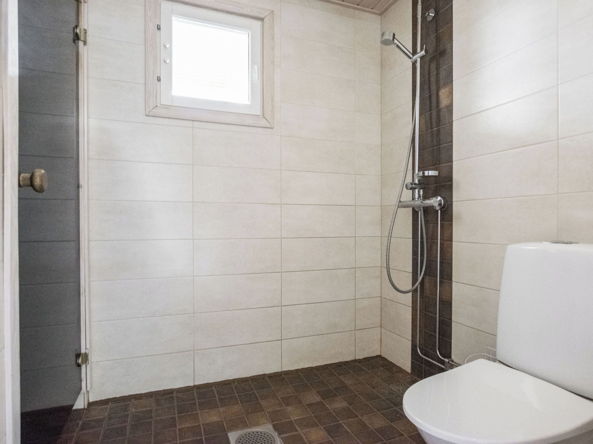 A bathroom with a shower, toilet, and a window.