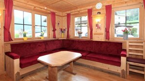 Ein gemütliches Blockhäuschen-Interieur mit Holzbalkendecke, roten Vorhängen, einer hölzernen Bank und einem Tisch.