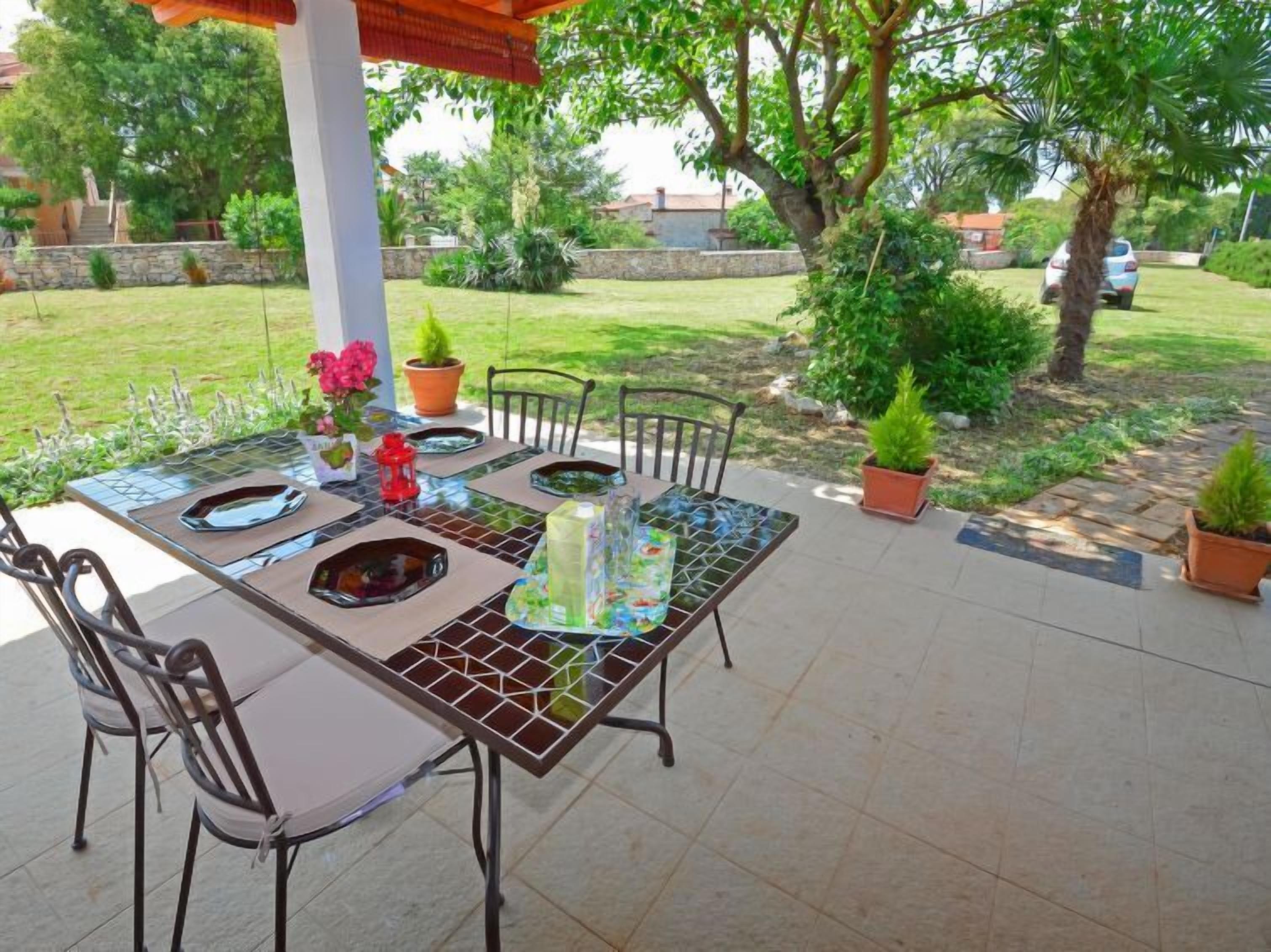 An outdoor patio with a glass-top table, metal chairs, and potted plants.